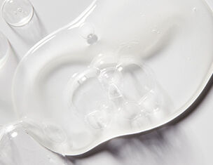 A clear, smooth gel-like substance spread across a white surface, reflecting light and creating subtle shadows.