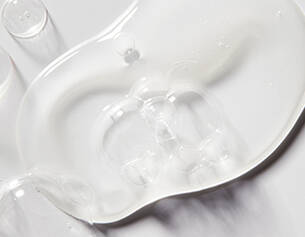 A clear, smooth gel-like substance spread across a white surface, reflecting light and creating subtle shadows.