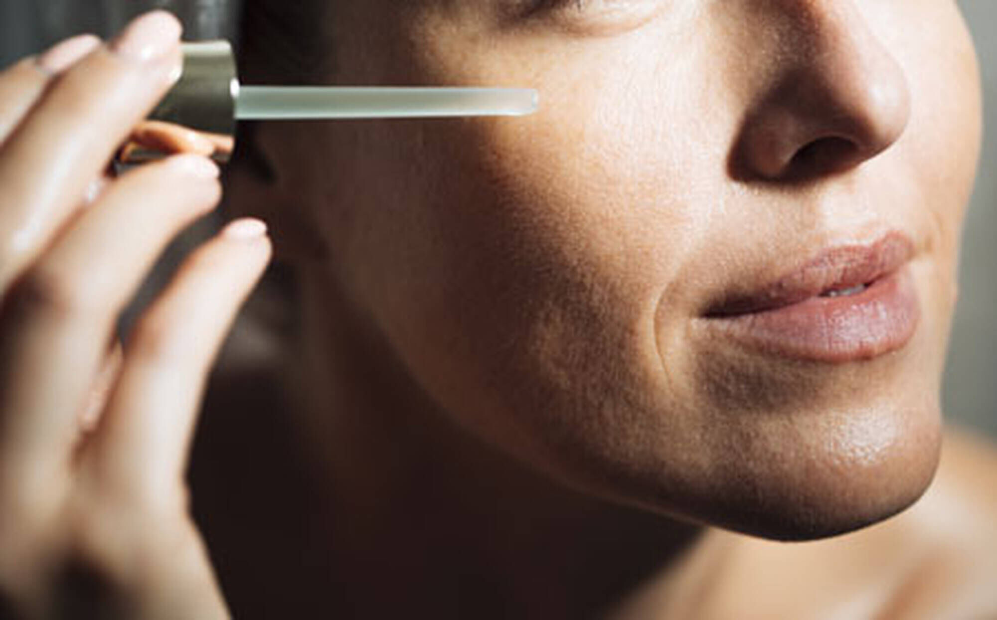 Femme appliquant un serum sur son visage, mettant en avant sa peau douce et lumineuse.