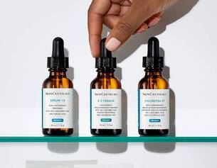 Main dans un flacon de serum, trois bouteilles de soins de la peau SkinCeuticals sur une etagere blanche.