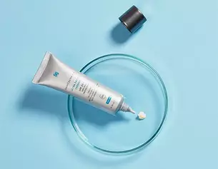 Tube de creme hydratante sur un plat en verre transparent, pose sur un fond bleu. Une petite quantite de creme est extraite.