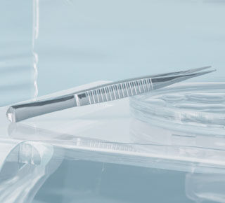 A close-up view of a dental or medical instrument, specifically a stainless steel tweezers, resting on a clear surface, with soft lighting and blurred background.
