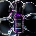 Un flacon de serum SkinCeuticals H.A. Intensifier entoure de bulles iridescentes.