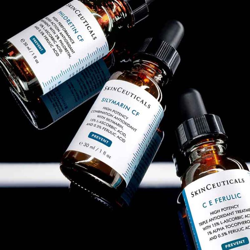 Trois flacons de serum a la vitamine C de SkinCeuticals, sur un fond sombre et reflechissant.