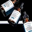 Trois flacons de serum a la vitamine C de SkinCeuticals, sur un fond sombre et reflechissant.