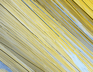 Close-up of long, thin yellow and gray wooden planks arranged diagonally, creating a textured and colorful pattern.
