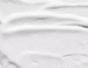 Texture lisse d&aposune creme blanche etalee sur une surface, mettant en evidence des ondulations delicates.