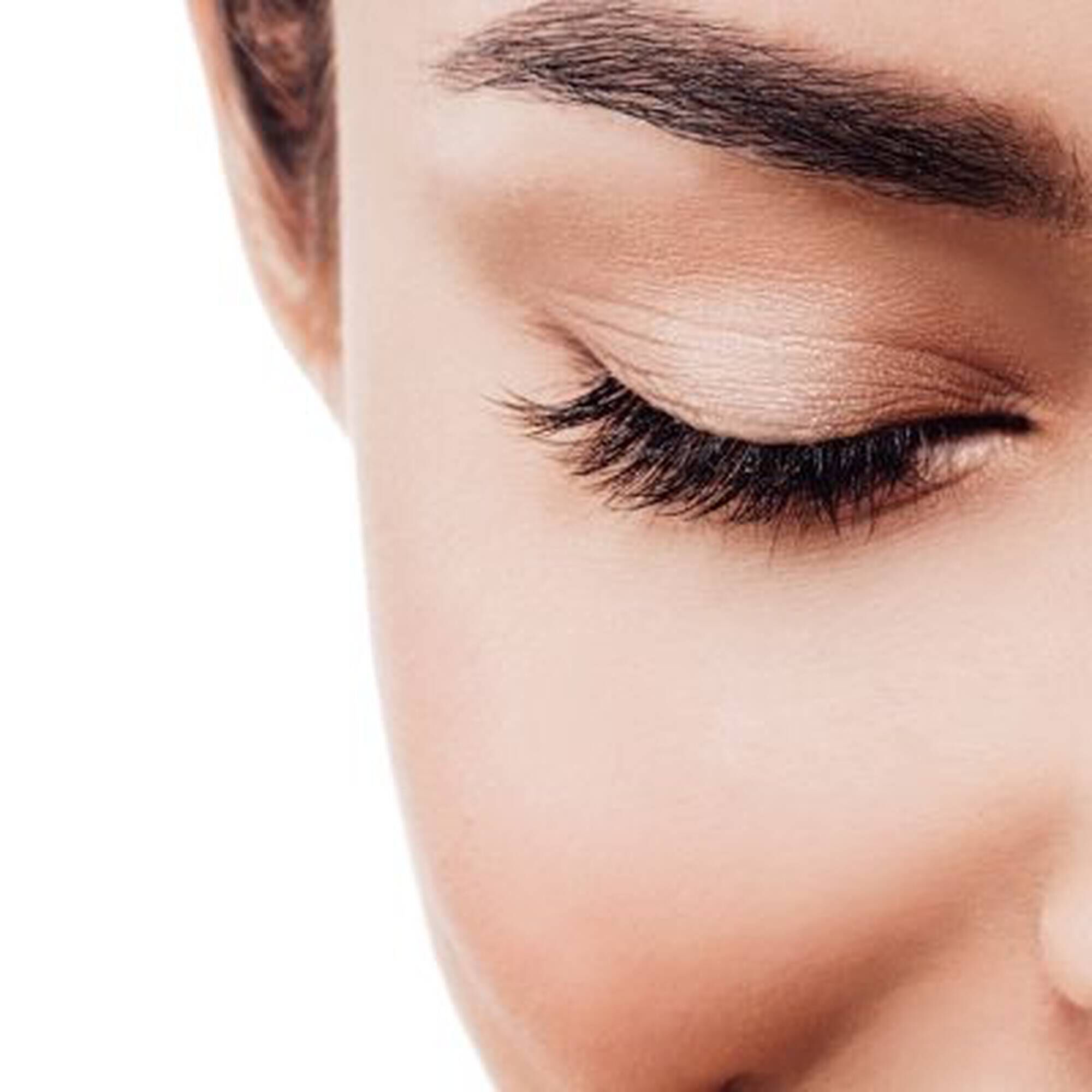 Gros plan sur un oeil feminin avec des cils longs et une peau douce, sur fond blanc.