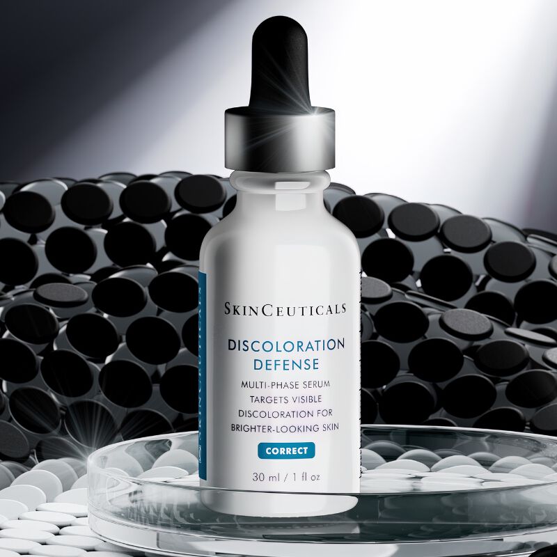 Flacon de serum SkinCeuticals Discoloration Defense sur une surface reflechissante, sur un fond sombre et texture