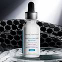 Flacon de serum SkinCeuticals Discoloration Defense sur une surface reflechissante, sur un fond sombre et texture