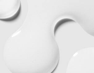 Gouttes de peinture blanche sur fond gris, illustrant une texture lisse et brillante.