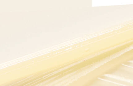 A close-up of a smooth, creamy substance with a light beige color, set against a soft, neutral background.