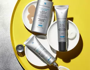 Trois produits de soin de la peau de SkinCeuticals sur des assiettes blanches, poses sur un fond jaune vif.