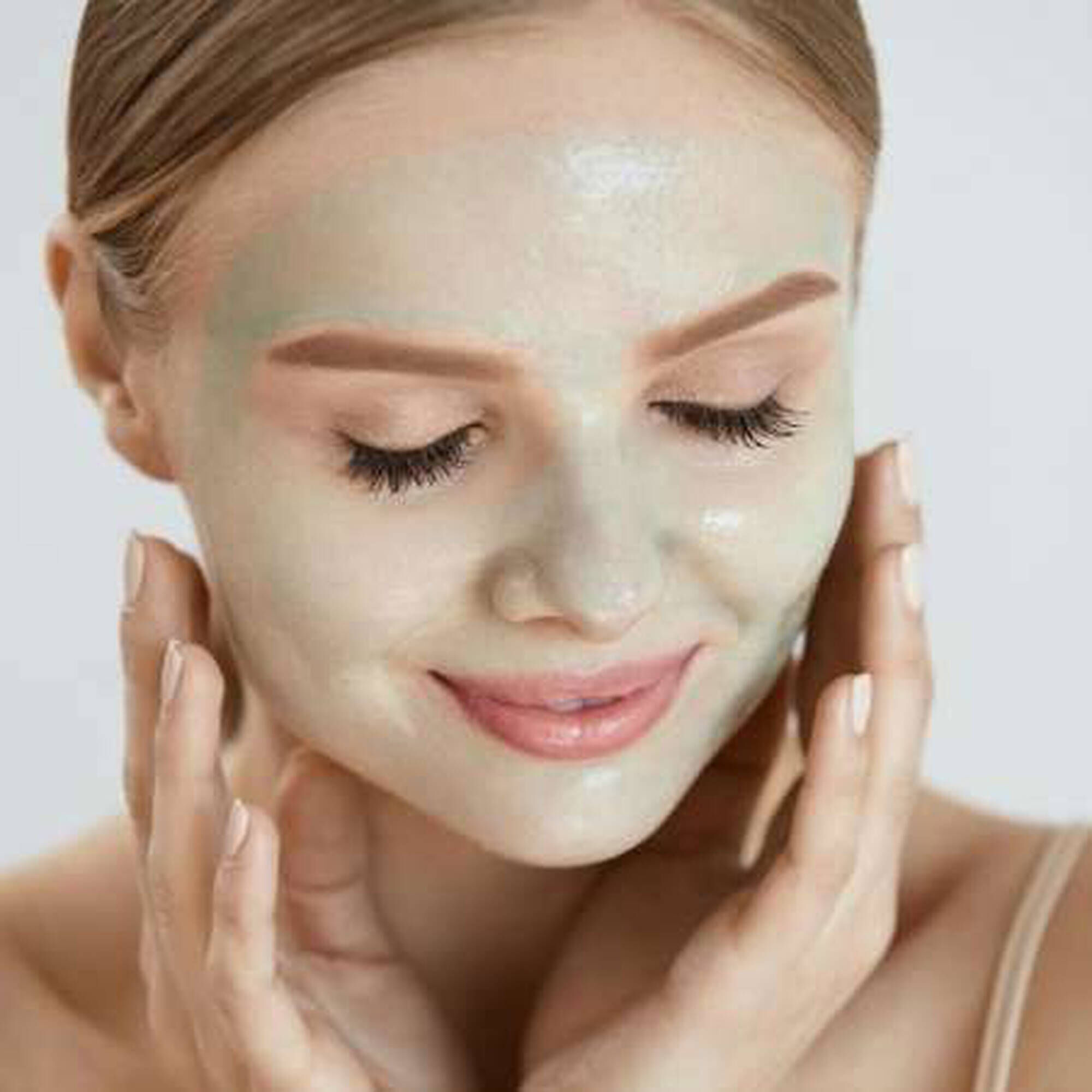 Femme souriante avec un masque facial vert applique, prenant soin de sa peau.