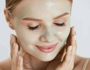 Femme souriante avec un masque facial vert applique, prenant soin de sa peau.