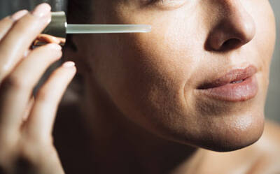 Une femme applique un serum sur son visage avec un compte-gouttes.