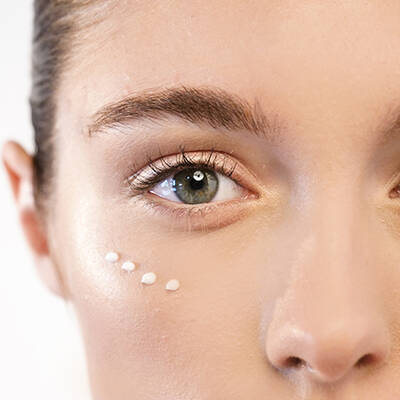 Un gros plan sur un oeil humain avec une creme appliquee sous l'oeil. La peau est lumineuse et naturelle.
