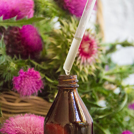 Flacon en verre brun avec une pipette, pres de fleurs violettes.