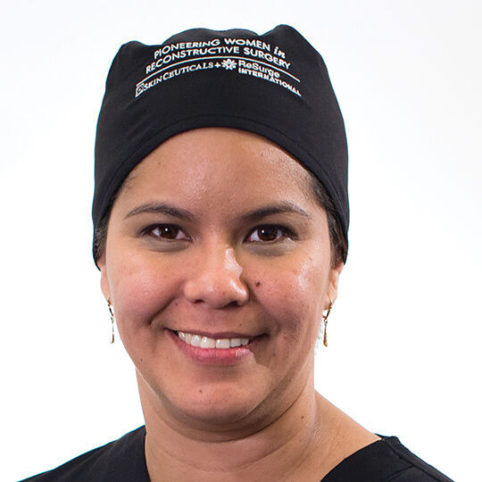 Une femme souriante portant un bonnet noir avec un logo, sur un fond blanc.