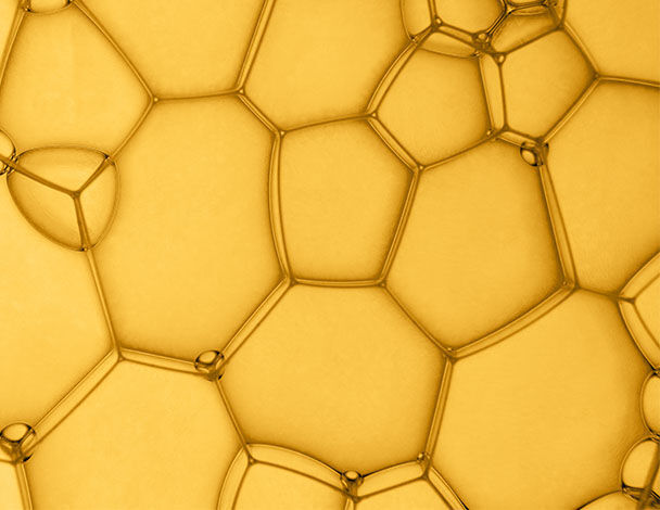 Des bulles de savon en forme de hexagones, brillantes, sur fond jaune, creant un motif vibrant et delicat.