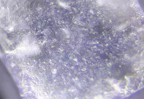 Vue rapprochee d’un cristal transparent presentant des imperfections de surface et des bulles, eclaire au microscope.