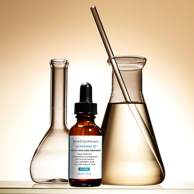 Un flacon de serum SkinCeuticals "Silymarin CF" avec des flacons et un tube en verre, le tout sur un fond lumineux.