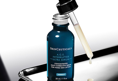 Flacon de serum SkinCeuticals C E Ferulic avec gouttelette, sur fond clair, entoure de gouttes d'huile.