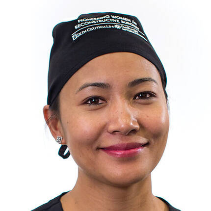 Portrait d'une femme souriante portant un chapeau de medecin, sur fond blanc.