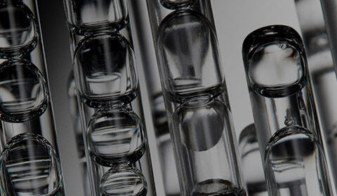 Gros plan d'un compte-gouttes transparent distribuant quelques gouttes de serum sur une surface blanche
