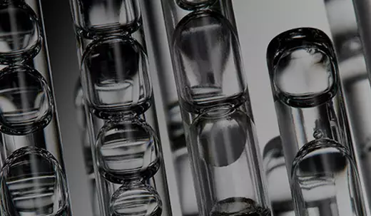 Gros plan d'un compte-gouttes transparent distribuant quelques gouttes de serum sur une surface blanche
