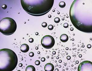 Close-up of iridescent bubbles of varying sizes floating against a soft purple background.