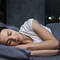 Une femme dort paisiblement dans un lit, souriante, avec un eclairage doux de la nuit a travers la fenetre.