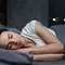 Une femme dort paisiblement dans un lit, souriante, avec un eclairage doux de la nuit a travers la fenetre.