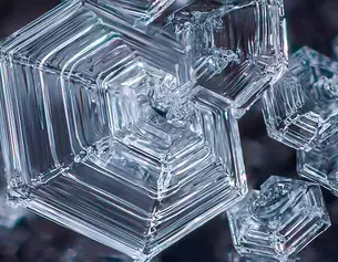 Gros plan de cristaux de glace transparents et complexes, dont les formes hexagonales se detachent sur un fond sombre.