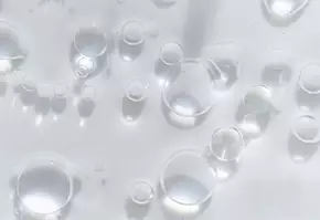 Gouttes d'eau en suspension sur une surface translucide, creant un effet de lumiere douce et de texture delicate.