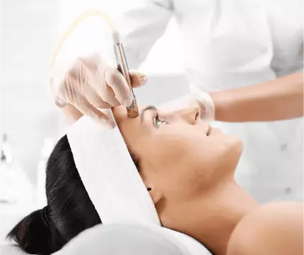 Une femme recevant un soin du visage dans un institut de beaute, avec un praticien utilisant un appareil esthetique.