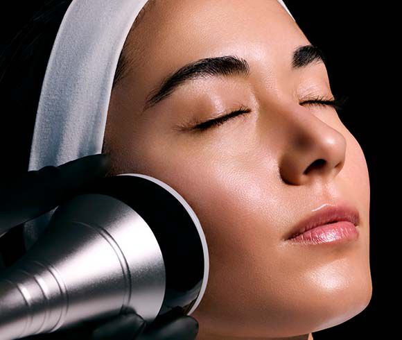Femme allongee lors d'un soin esthetique, portant une protection oculaire, avec un appareil laser au-dessus d'elle.