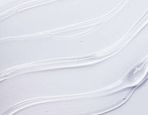 White creamy texture with smooth, flowing lines on a light background, resembling a skincare or cosmetic product.