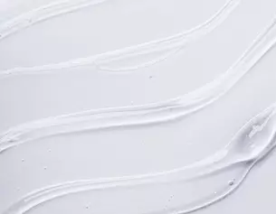 Texture cremeuse blanche aux lignes fluides et douces sur un fond clair, evoquant un produit de soin de la peau ou un cosmetique.