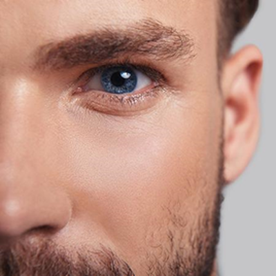 Un gros plan d'un oeil bleu d'un homme avec une barbe bien taillee et une peau claire.