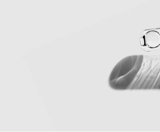 Gros plan d'un compte-gouttes transparent distribuant quelques gouttes de serum sur une surface blanche