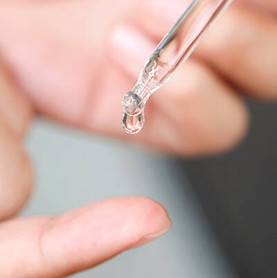 Un compte-gouttes transparent deverse une goutte de liquide sur un doigt.