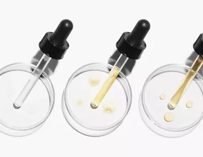 Trois pipettes avec des serums de differentes couleurs reposent sur des dishes de Petri transparentes.