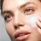 Femme en train d'appliquer une creme sur son visage, mettant en valeur sa peau eclatante et ses yeux clairs.