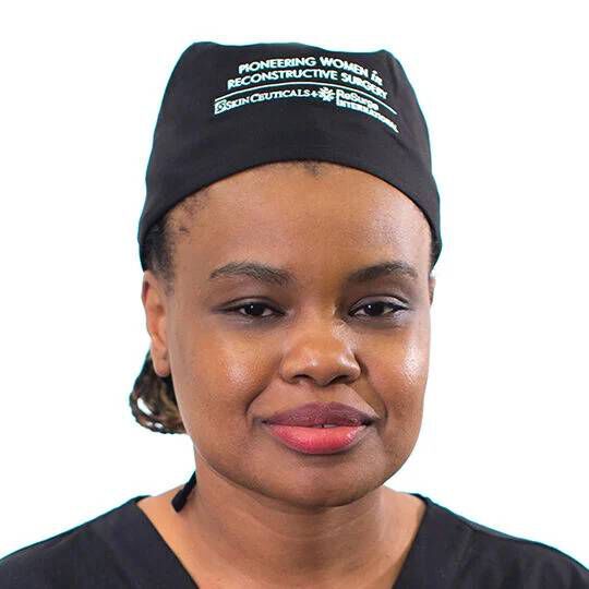 Une femme portant une tenue medicale et un bonnet noir, regardant vers l'objectif avec une expression calme.