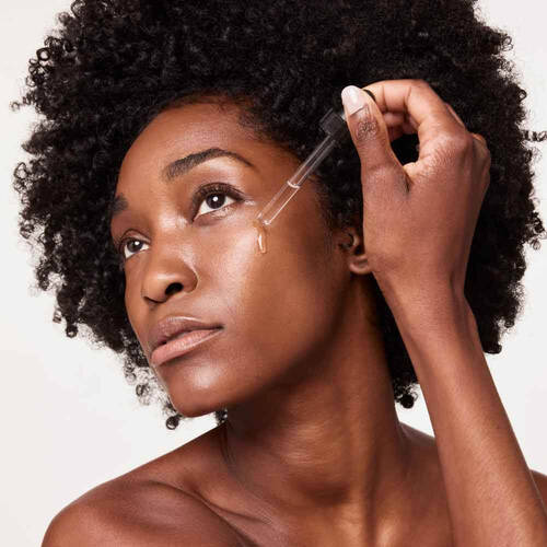 Femme avec des cheveux boucles utilisant un compte-gouttes pour appliquer un serum sur le visage.