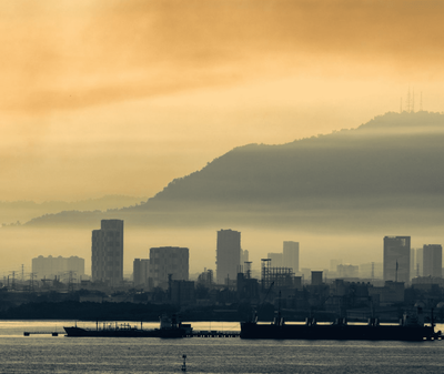 Silhouette d'un paysage urbain au crépuscule, avec des bateaux et des collines en arrière-plan sous un ciel doré.